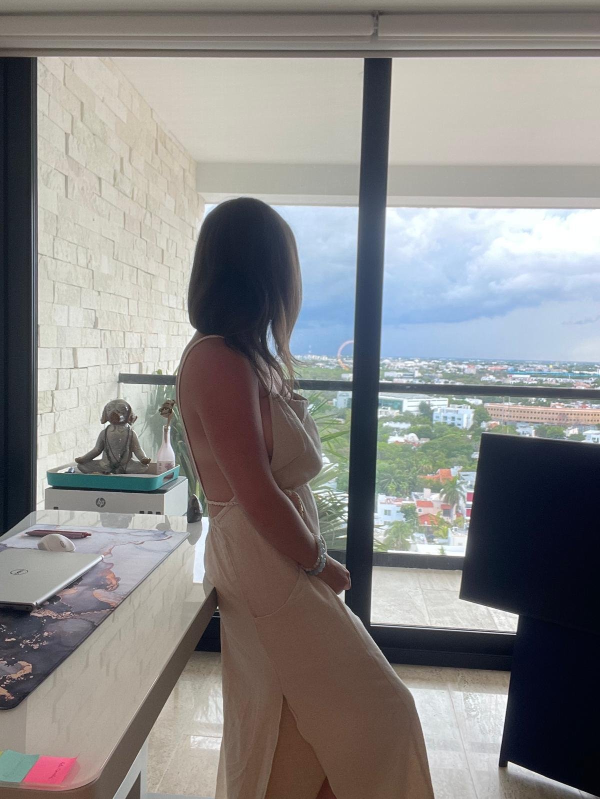 Jenna Jade beside a home-office window overlooking the city.