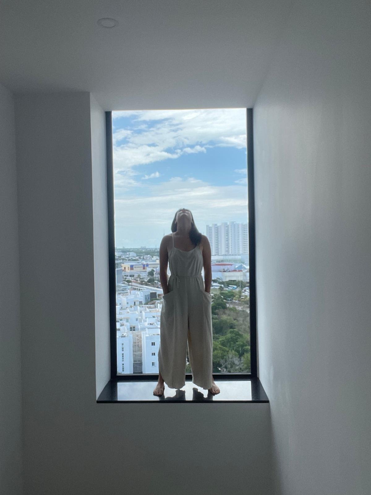 Jenna Jade looking upward while standing in a tall window alcove.